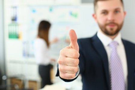 Businessman showing thumb up sign of success over blurred team of business peopleの写真素材