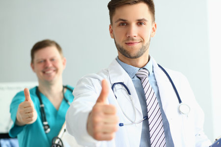 Two doctors gesture thumbs up in clinic recommending medical servicesの写真素材