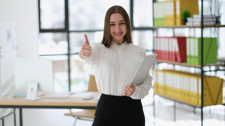 Businesswoman showing thumbs up at work in officeの写真素材