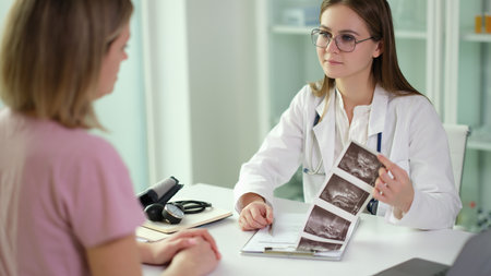 Doctor communicating with patient and examining results of ultrasound examination of internal organs in clinicの写真素材