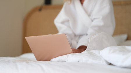 Woman in white bathrobe sitting with laptop in bed at home closeupの写真素材