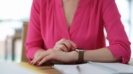 Business woman adjusting wrist watch at table in office closeup