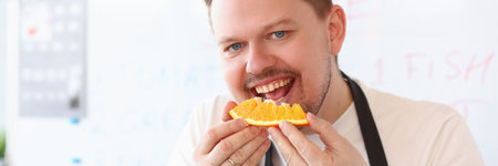 Red smiling male cook is biting orangeの写真素材