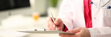 Woman medicine doctor with silver pen writes on a clipboard closeup.の写真素材
