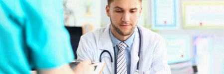 Male doctor carefully examines documents in office of clinic at workplaceの写真素材