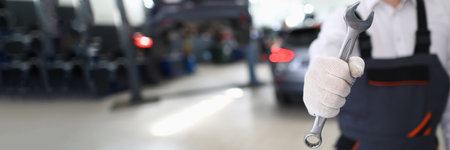 Car repairman in uniform holds wrench in car workshopの写真素材