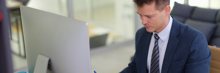 Businessman studying paper document in front of computer in officeの写真素材