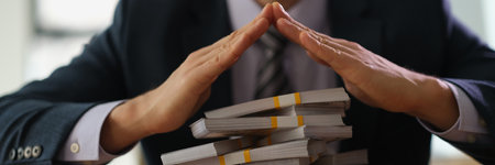 Banker making roof with hands over bundles of dollar bills closeupの写真素材