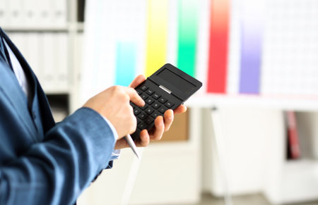 Male arm in suit hold calculator pressing buttonsの写真素材