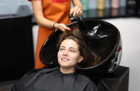 Master washes her hair in sink for client in hairdressing salonの写真素材