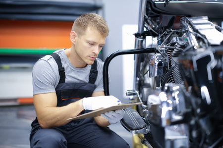 Young car mechanic conducts diagnostics of motorcycle engine in car service