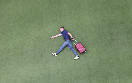 Young man with suitcase walking on green grass top view