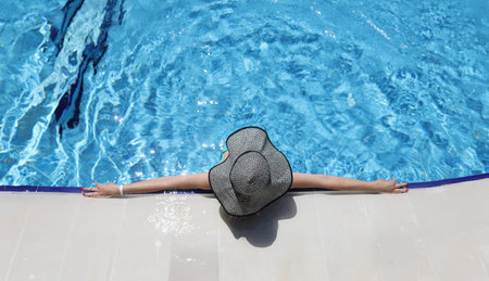 Woman in panama lying on edge of swimming pool top view