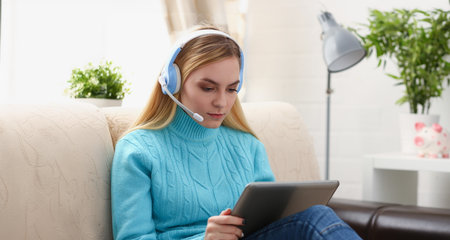 young beautiful blond woman sit on the sofa in livingroom hold tablet in arms listen to music sunnyの写真素材