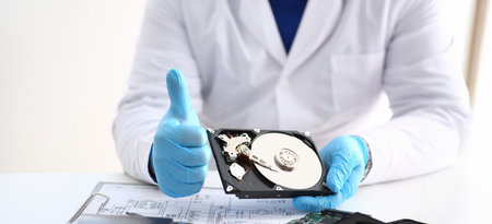 Man in uniform hold disassembled hard drive from computer, hdd and reader, show thumbs up