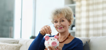 An elderly woman puts a coin in a piggy bankの写真素材