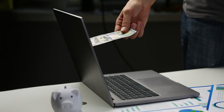 Man invest money through computer screen, put banknote to online bankの写真素材