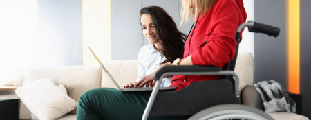 Best friends spend time together watching movie on laptop, woman in wheelchair hold device on lapの写真素材