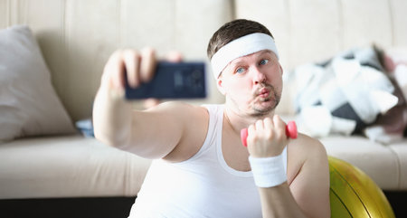 Sportsman training at home lifting dumbbell and take selfie for social media channelの写真素材