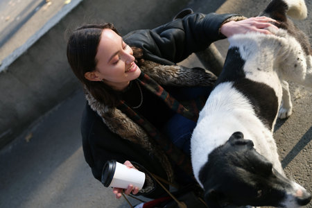 A Young Woman is Gently Petting a Cute Dog in a Lively Urban Setting Surrounded by Many Peopleの写真素材