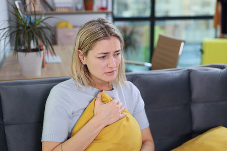 Woman sitting on a couch holding a pillow, lost in thought during a quiet afternoon at home