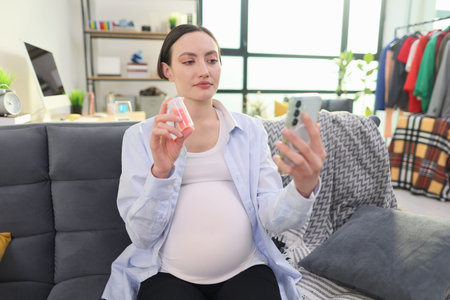 Expectant mother relaxing on a couch while checking her phone for pregnancy tips and products in a...