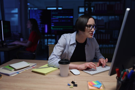 Focused programmer immersed in late-night coding session at a dimly lit workspace with a cup of...