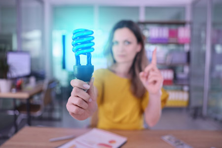Creative woman holds glowing blue light bulb while emphasizing a great idea in a modern office space...