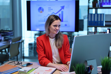Business professional works on computer in modern office with growth charts displayed in background