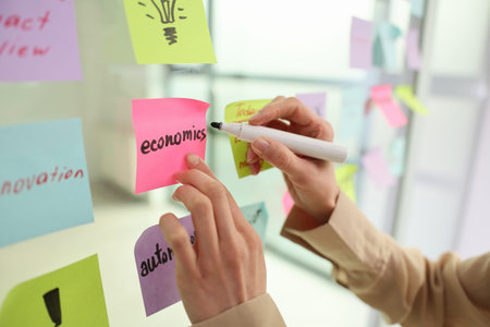 Hands are writing ideas on colorful sticky notes for a creative brainstorming session in a bright...
