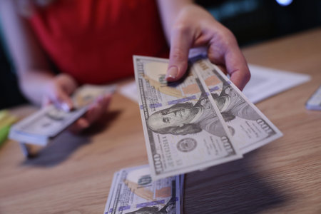 Person exchanging money with a stack of cash visible on the table during a busy transaction in a...