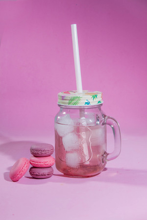 Colorful french macarons cookies. French pastry on a pink background, minimal concept. Lots of macaroons. Raspberry lemonade with ice in a glassの写真素材