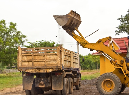 Yellow bulldozer was scooping soil into the truck  in bad weather 