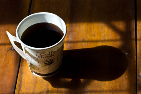 a paper cup of black coffee on wooden table
