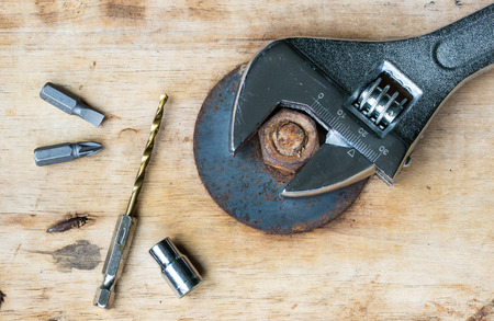 Pliers Drill, screwdriver and nut on a wooden floor.