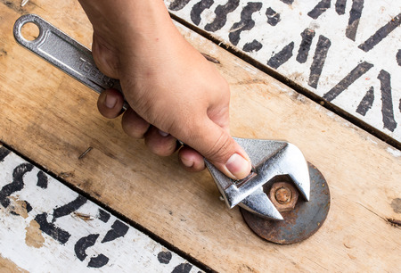 hand holds wrench and tighten the nut on the wooden floor.