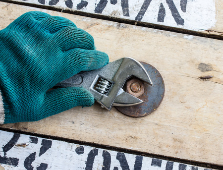 hand holds wrench and tighten the nut on the wooden floor.の写真素材