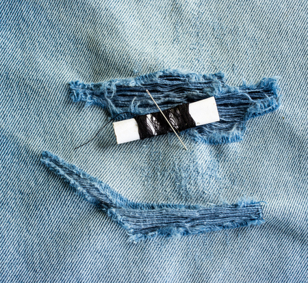 Threads and needle on jeans backround, wear repair concept