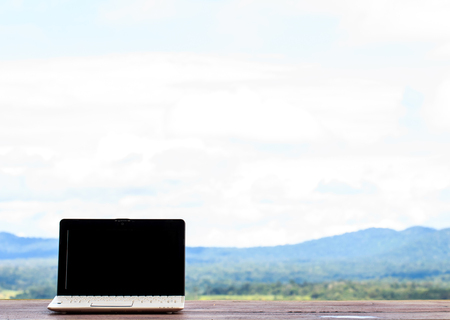 Laptop stands on a wooden table outdoors and nature backgroundの写真素材