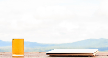 Glass beer on wood table and laptop on mountain nature backgroundの写真素材