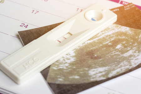 Positive white plastic pregnancy test and calendar with ultrasound of baby in pregnant woman at three month.の写真素材