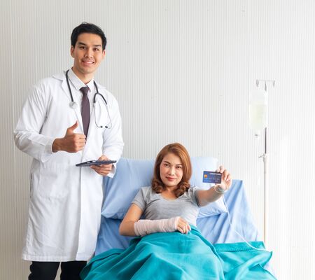 The female patient in the bed carried a credit card, with a young doctor standing there to support by the bed.の写真素材