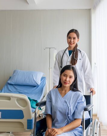 An Asian female doctor cheered on a female patient in a wheelchair in her room.の写真素材