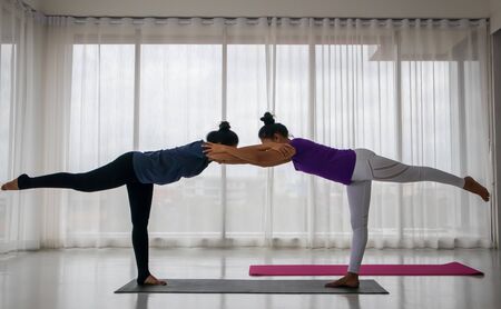 Teacher teach student to do yoga concept. A middle-aged Asian woman is teaching another woman to do yoga in a stretching position, where the teacher comes to catch the right posture.の写真素材
