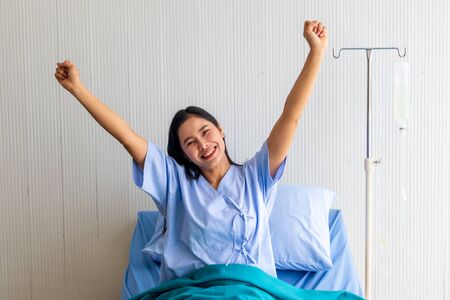 Young Asian patient woman lying at hospital bed with saline sign for cheerful. Drop of saline solution to help patient.の写真素材
