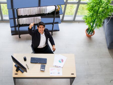 A young Asian businessman sitting on a chair in a comfortable position at the officeの写真素材