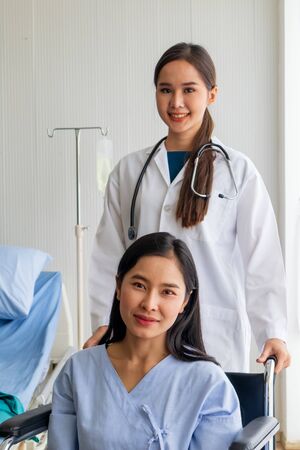 An Asian female doctor cheered on a female patient in a wheelchair in her room.の写真素材