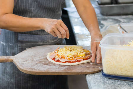 people and cooking concept - cook hand adding grated cheese to pizza at pizzeriaの写真素材