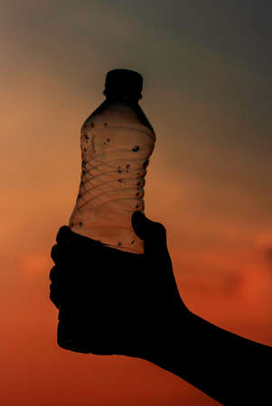 Hand holding bottle water on sunset sky,Summer holiday vacation outdoor and view in evening,Drinksの写真素材