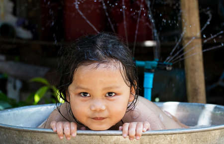 Happy children girl bath in plastic basin in nature and play in the water. outdoor water treatments.の写真素材